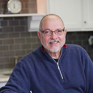 A man sitting in front of a kitchen wall.