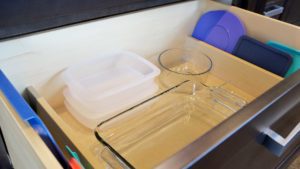 A drawer with some plastic containers and a glass