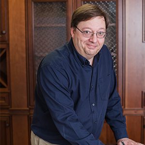 A man in glasses and blue shirt leaning on a table.