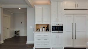 A kitchen with white cabinets and drawers, coffee maker in the center of the cabinet.