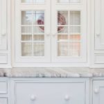 A white cabinet with two glass doors and a marble counter top.