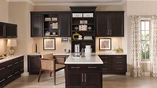 A kitchen with dark wood cabinets and white counter tops.