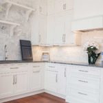 A kitchen with white cabinets and marble backsplash.