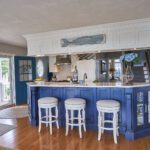 A kitchen with blue cabinets and white stools.