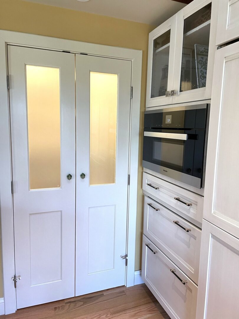 A white kitchen with two doors and a microwave.
