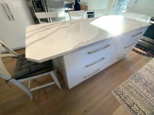A kitchen island with white cabinets and marble counter tops.