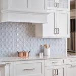 A kitchen with white cabinets and a blue backsplash.