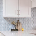 A kitchen with white cabinets and blue patterned tile.