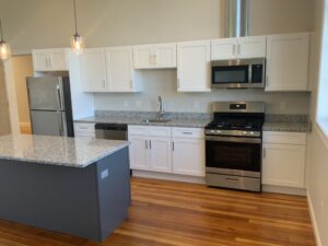 Modern kitchen interior with white cabinetry, stainless steel appliances, and a central island with a gray countertop.