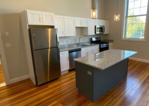 Modern kitchen interior with stainless steel appliances, white cabinets, and a central island with a granite countertop.