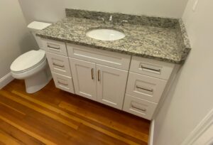 A modern bathroom with a white vanity cabinet, granite countertop, and an undermount sink beside a white toilet.