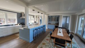 A spacious kitchen with a blue island, wooden floors, and modern appliances, connected to a dining area with a wooden table.