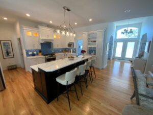 A modern kitchen with white cabinetry, blue tile backsplash, and a central island with bar seating.