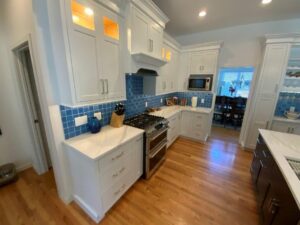 A modern kitchen with white cabinetry, blue tile backsplash, stainless steel appliances, and hardwood flooring.