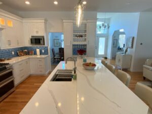 A modern kitchen with white cabinetry, blue backsplash, and a marble countertop island.