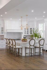 White kitchen island with bar stools and gold lights.