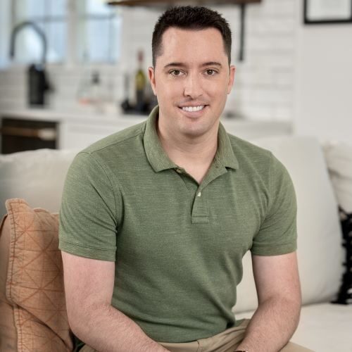 Cropped Greg Resized A man sitting on top of a couch in front of a window.